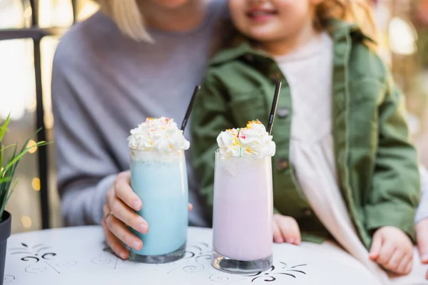 Abgeschnittene Ansicht von verschwommener Mutter und Tochter in der Nähe von Gläsern mit Milchshake und Schlagsahne — Stockfoto