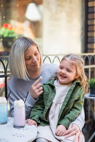 Lächelnde Frau mit leckerer Schlagsahne am Finger sitzt mit Tochter im Café auf der Straße — Stockfoto
