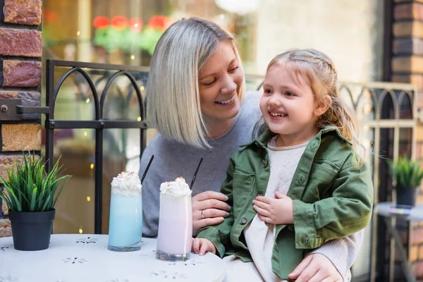 Menina satisfeito tocando barriga perto de óculos com delicioso milkshake e mãe — Fotografia de Stock