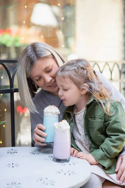 Niño pequeño disfrutando de delicioso batido cerca de la mamá en la cafetería al aire libre - foto de stock