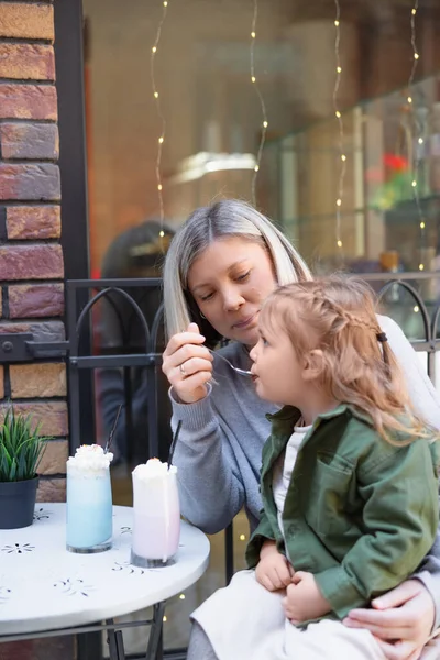 Glückliche Frau füttert Tochter mit Milchdessert in Café an der Stadtstraße — Stockfoto