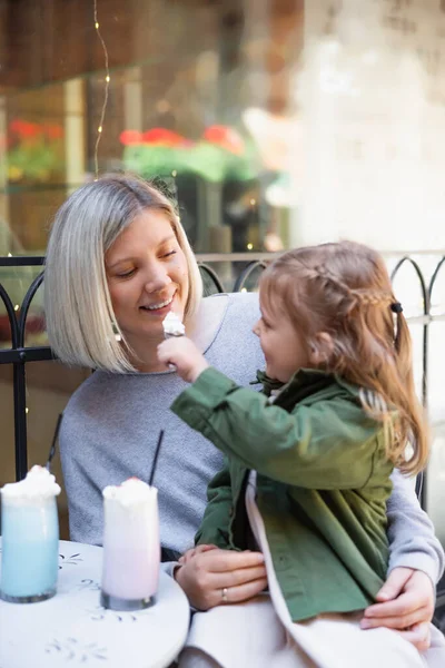 Kleines Kind füttert glückliche Mutter in Café an der Stadtstraße mit Schlagsahne — Stockfoto