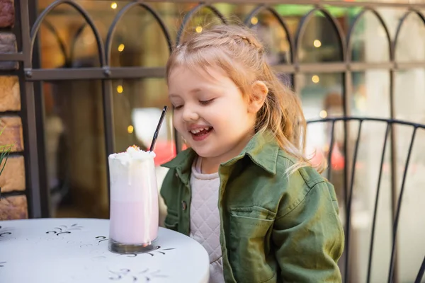 Cheerful girl sitting near milkshake while sitting outdoors — Stockfoto