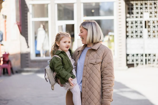 Amazed blonde woman holding little daughter on city street — Stock Photo