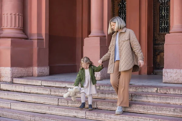 Mother and daughter with teddy bear walking on stairs outdoors — Photo de stock