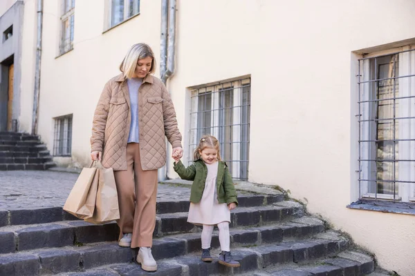 Woman with shopping bags holding hands with daughter while walking on stairs outdoors — Stock Photo