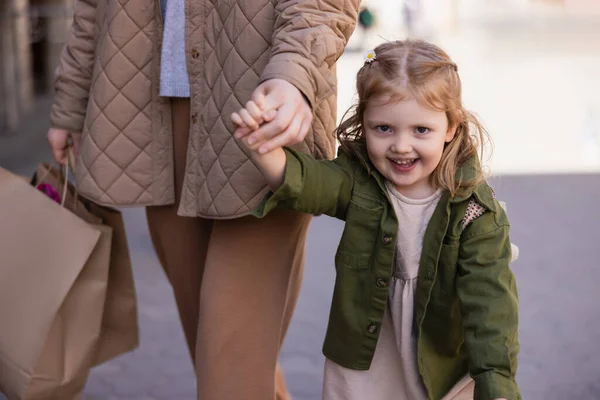 Excited girl holding hands with mother carrying shopping bags outdoors — Stockfoto