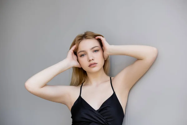 Jeune femme élégante touchant les cheveux et regardant la caméra sur fond gris — Photo de stock