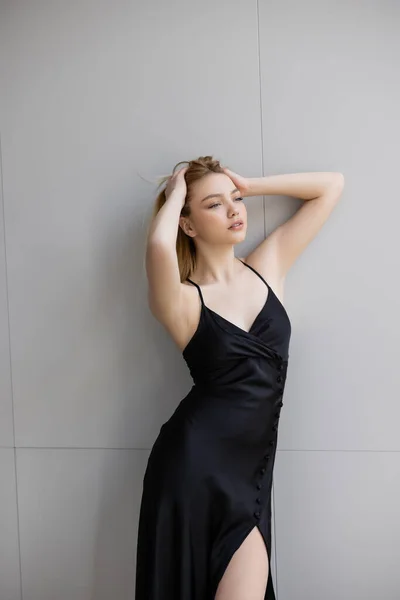 Mujer elegante tocando el cabello mientras está de pie cerca de la pared - foto de stock