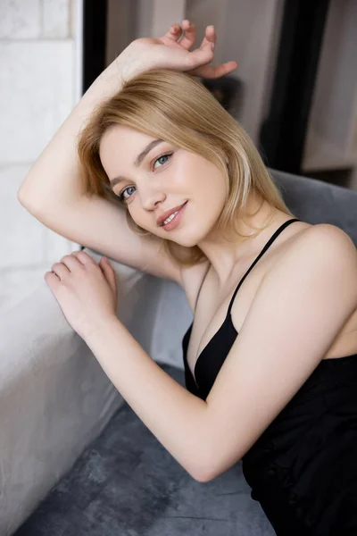 Smiling young woman in dress looking at camera on couch — Stock Photo