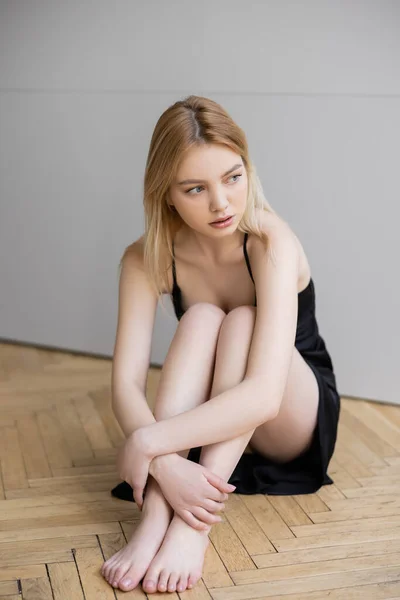 Junge Frau in schwarzem Kleid sitzt zu Hause auf Holzboden — Stockfoto