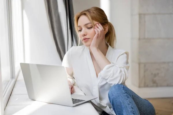 Young woman using laptop on windowsill at home — Stock Photo