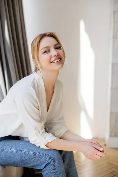 Mujer feliz en jeans y blusa mirando a la cámara en casa - foto de stock