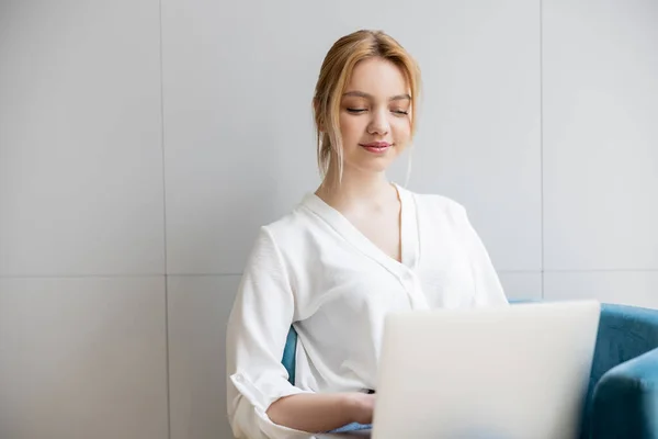 Junge Frau in Bluse mit Laptop auf Sessel zu Hause — Stockfoto