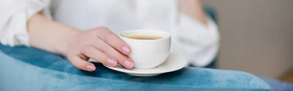 Vista ritagliata della donna che tiene la tazza di caffè sul piattino sulla poltrona, banner — Foto stock