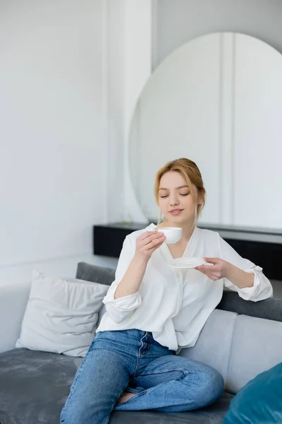 Femme blonde en jeans et chemisier tenant une tasse de café dans le salon — Photo de stock