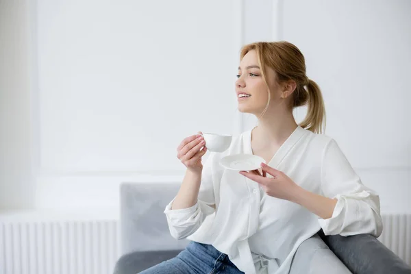 Hübsche Frau in weißer Bluse hält Tasse Kaffee im Wohnzimmer — Stockfoto