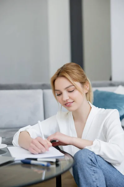 Positive Frau in Bluse schreibt zu Hause auf Notizbuch — Stockfoto