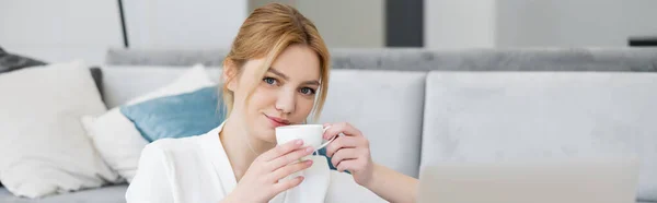 Junge Frau in Bluse mit Tasse Kaffee und Blick in die Kamera zu Hause, Banner — Stockfoto