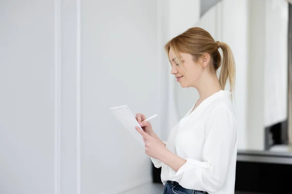 Вид збоку щасливої жінки в блузці, що пише на блокноті у вітальні — стокове фото