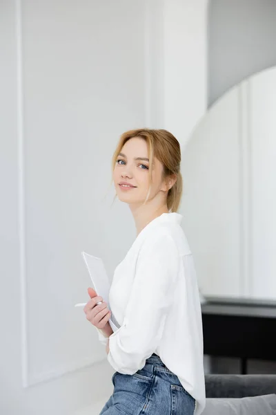 Retrato de mulher loira sorridente segurando caneta e caderno em casa — Fotografia de Stock