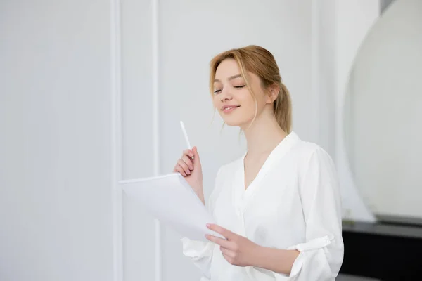 Blonde Frau in Bluse hält Stift und Notizbuch im Wohnzimmer — Stockfoto
