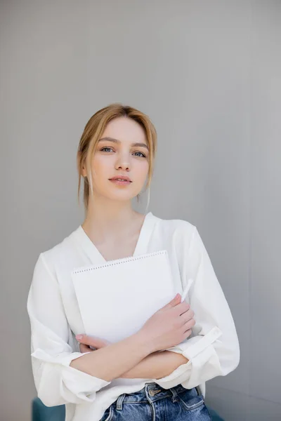 Portrait of young woman in blouse holding notebook and looking at camera at home — Stock Photo