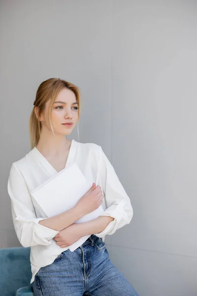 Mulher de jeans e blusa segurando caderno em casa — Fotografia de Stock