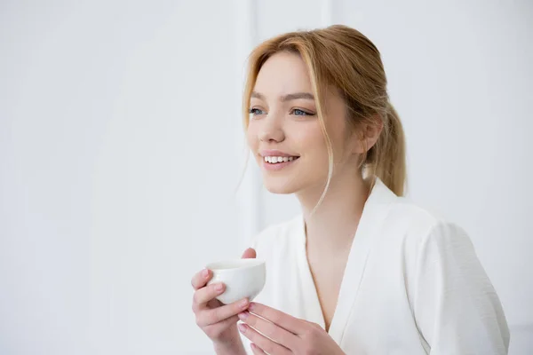 Pretty young woman holding cup and looking away at home — Stock Photo