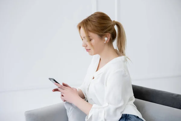 Красива молода жінка в навушниках, використовуючи мобільний телефон на дивані вдома — стокове фото