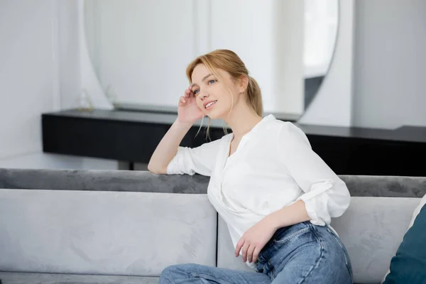 Fröhliche Frau in weißer Bluse sitzt auf Couch im Wohnzimmer — Stockfoto