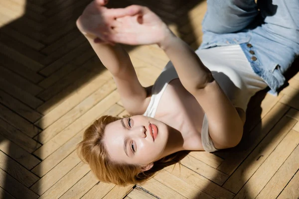 Positive junge Frau, die am Boden liegend in die Kamera blickt — Stockfoto