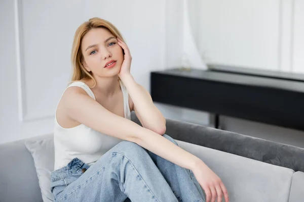 Schöne blonde Frau in Jeans sitzt zu Hause auf dem Sofa — Stockfoto