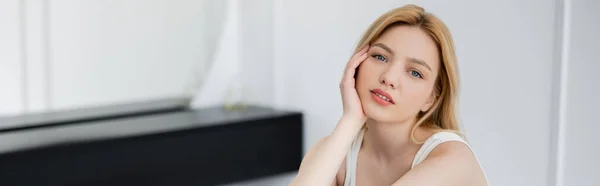 Portrait of young woman holding hand near cheek and looking at camera, banner — Stock Photo