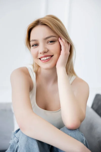 Ritratto di giovane donna positiva che guarda la macchina fotografica sul divano sfocato — Foto stock