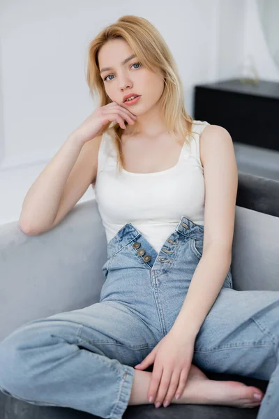 Jolie femme en body et jeans posant sur le canapé — Photo de stock