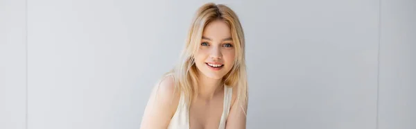 Retrato de mujer rubia sonriendo a la cámara cerca de la pared gris, pancarta - foto de stock