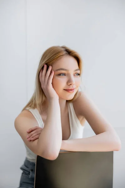 Mujer joven y bonita sentada en la silla y sonriendo en casa - foto de stock