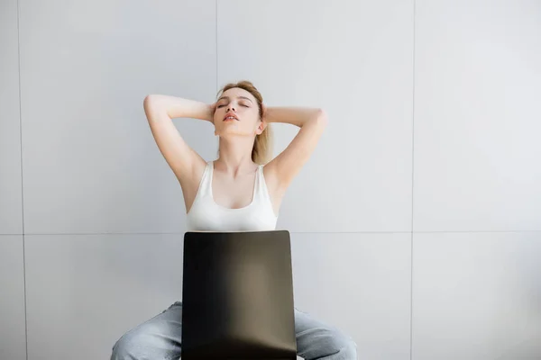 Hübsche Frau mit geschlossenen Augen, die das Haar berührt, während sie zu Hause auf einem Stuhl sitzt — Stockfoto