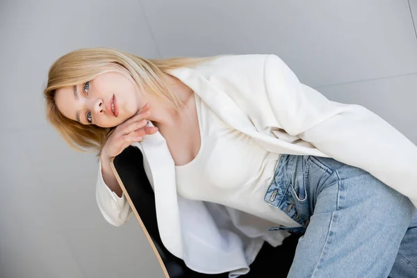 Donna bionda in giacca bianca e jeans seduta sulla sedia a casa — Foto stock