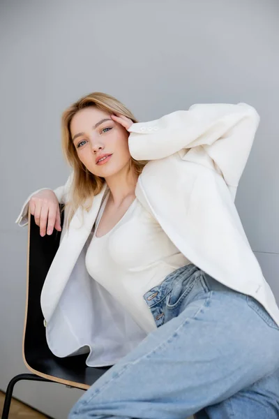 Mujer de moda en jeans y chaqueta mirando a la cámara en la silla - foto de stock