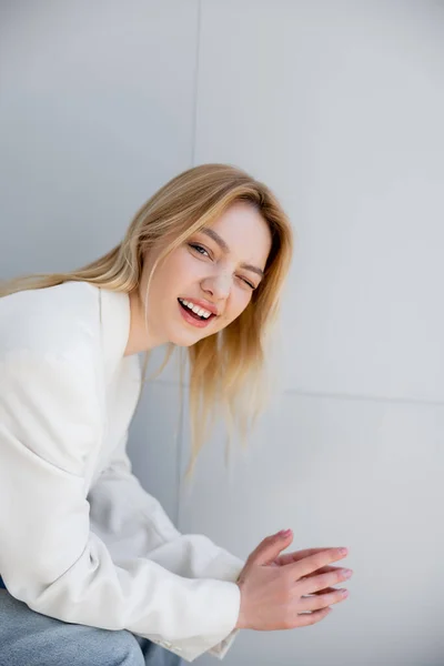 Blonde woman in jacket winking at camera at home — Stock Photo