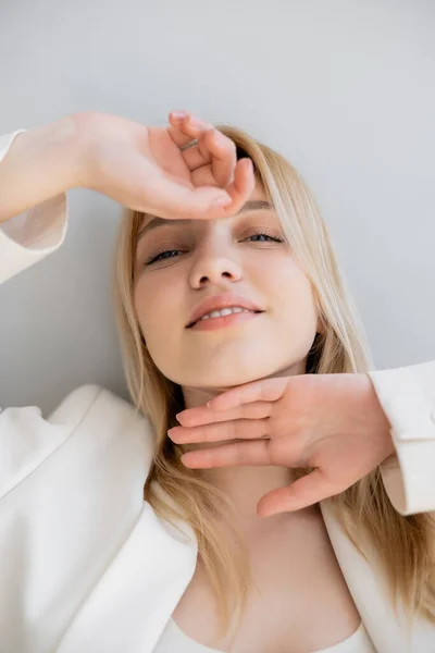 Porträt einer lächelnden blonden Frau im Sakko, die isoliert in die Kamera auf grau blickt — Stockfoto