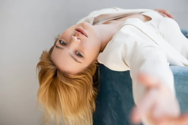 Mujer bonita con estilo en la chaqueta mirando a la cámara mientras está sentado en el sillón aislado en gris - foto de stock