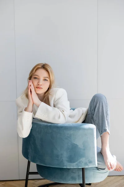 Femme élégante et pieds nus assise sur un fauteuil bleu à la maison — Photo de stock