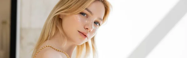 Blonde woman with glitter on cheeks posing at home, banner — Stock Photo