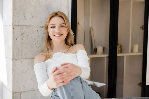 Glückliche junge Frau mit Glitzerschminke schaut zu Hause in die Kamera — Stockfoto