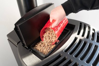 Close-up on pellets, black domestic pellet stove, man loading by hand granules with a red 3 d printed cup