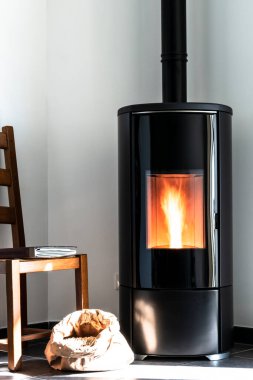 Modern black stove with burning flames and pellet bag in a living room