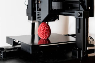 Close up of a 3d printer printing a red polygonal egg